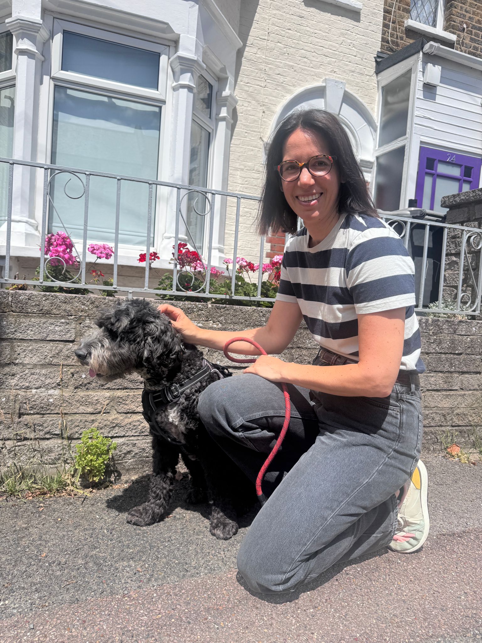 Simone kneeling on a garden path, smiling with her hand on her dog